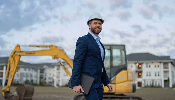 businessman inspect building plan at site. businessman checking building plan outdoor. photo of businessman with building plan wearing hardhat. businessman with building plan.