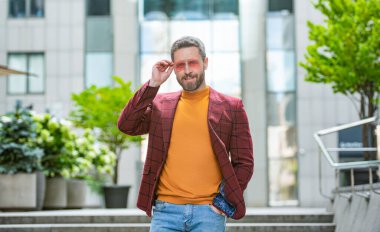 Dışarıda erkek giysili mutlu bir adam var. Ceketli bir adamın fotoğrafı. Açık havada erkek giyim bölümünde bir adam. Sokaktaki erkek giyim mağazası..