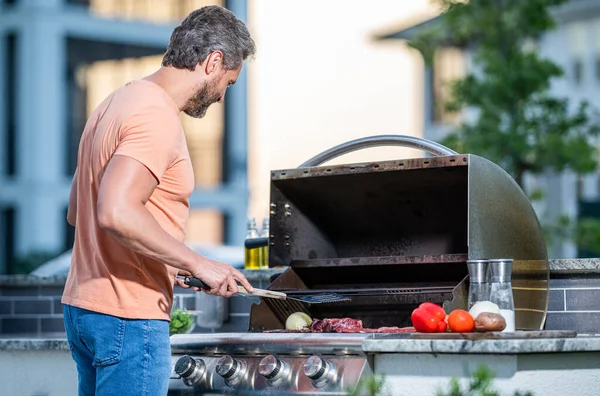 Man grilling steaks to perfection on smoky barbecue. Barbecue cooking prowess. Grilling man cook meat at barbecue. Outdoor man cooking grill and barbecue dishes.