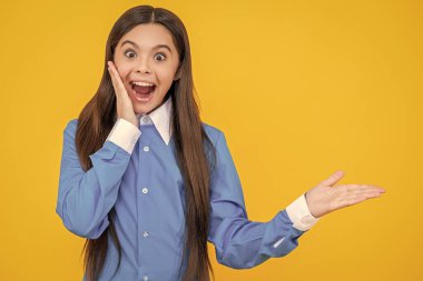 Üniforma giyen, ürün sunan genç bir kızın fotoğrafı. Genç liseli kız sarıda izole edilmiş. Stüdyodaki genç kız. Arka plandaki genç kız..