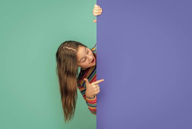 Reklam için fotokopi alanı olan boş mavi kağıdın arkasında şok olmuş bir çocuk. işaret parmağı.