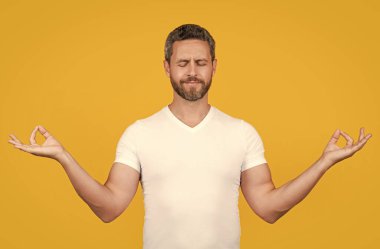 Sakallı adam, sarı gömlekle meditasyon yapıyor. Meditasyon stüdyosunda meditasyon yapan bir adam. Meditasyon yapan adamın beyaz gömlekli fotoğrafı. Adam günlük kıyafetlerle meditasyon yapıyor. meditasyon kavramı.