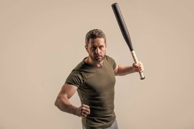 Olgun ve saldırgan bir adam. Adam gri arka planda kalan yarasalarla saldırganlığını ifade ediyor. Stüdyoda sopalı bir adamın saldırganlığı. Saldırgan bir adamın fotoğrafı..