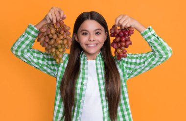 cheerful teen kid with grapes bunch on yellow background.