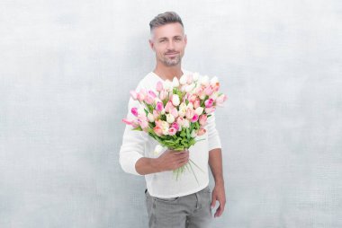 photo of man smile with valentines tulips. man with valentines tulips. man with valentines tulips in studio. man with valentines tulips isolated on blue background.