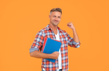 Heyecanlı erkek öğretmen, kitapları sarı arka plan ve eğitimle kazanma hareketi yapıyor..