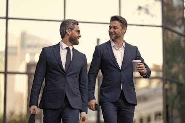 Gülümseyen takım elbiseli iş ortakları kahve molasında pazarlık ediyorlar. İş ortaklarının resmi ara verildiğinde görüşür. İş ortakları ara verildiğinde sokakta pazarlık yaparlar. İş ortakları ara verildiğinde görüşür