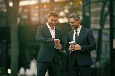 İşletme yöneticisi kontrol saati sokakta. İşletme yöneticisi dışarıda kontrol zamanı. Takım elbiseli bir işletme yöneticisi kahve tutuyor. İş yürütme denetim zamanının fotoğrafı.