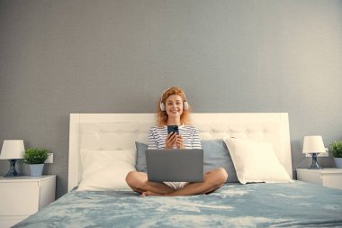 Neşeli kadın internette alışveriş yapıyor. Kadının evde telefonla alışverişi var. İnternetten kulaklıklı kadın alışverişi.