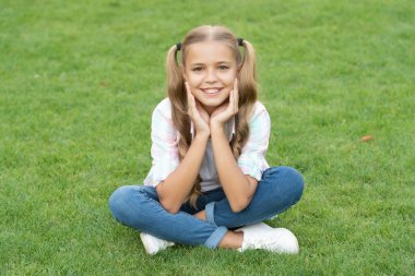 Genç kız dışarıda oturuyor. Gençliğin çocukluk tarzı. Yaz çimlerinde rahatla. Kız çimlerin üzerinde huzur içinde dinleniyor. Genç kızın mutlu çocukluğu. Yaz tatilinde parkta dinlenmek. Doğayla çevrili..