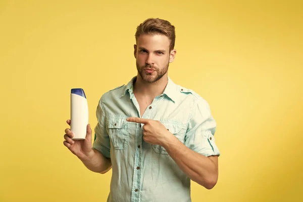 man pointing finger on aftershave cosmetics. man hold aftershave cosmetics isolated on yellow. man hold aftershave cosmetics in studio background. photo of man hold aftershave cosmetics.