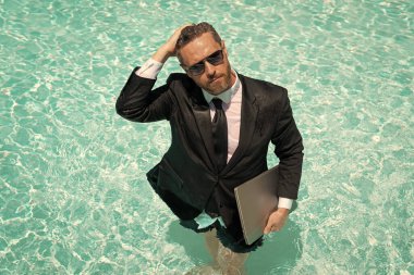 İş adamının yaz havuzunda dizüstü bilgisayarla uzaktan çalışma görüntüsü.