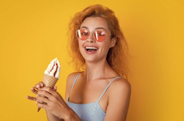 Dondurmalı gülümseyen kadın sarıda izole edilmiş. Stüdyoda dondurmalı bir kadın var. Arka planda dondurma külahı olan kadın. Yazın külahta dondurmalı bir kadının fotoğrafı..