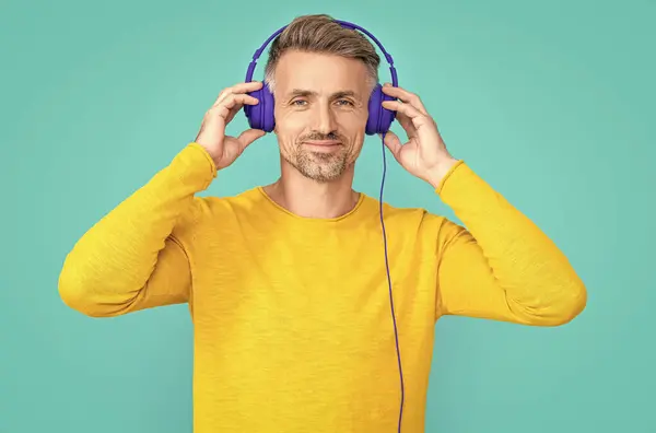 glad man listen music in headphones isolated on blue. man listen music in headphones at studio. man listen music in headphones on background. photo of man listen music in headphones.