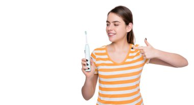 Tebessüm eden genç kadın, beyaz arka planda izole edilmiş elektrikli diş fırçasında işaret ediyor..