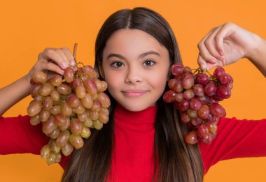 smiling teen girl hold bunch of grapes on yellow background.