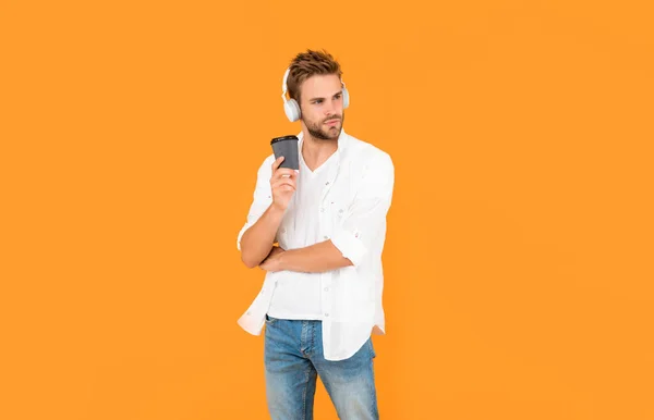 young man in modern earphones with coffee cup. online education. back to school. young guy in headphones drink coffee. music lover. listen to music. wireless device accessory. new technology.