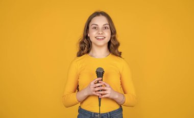 happy teen child with microphone on yellow background.