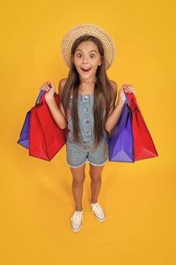 Sarı arka planda alışveriş torbaları olan afallamış genç bir çocuk..