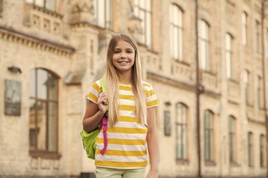 Happy teenage girl with backpack standing at school blurry outdoors, education.
