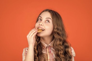 positive teen girl eating oatmeal cookies on orange background.