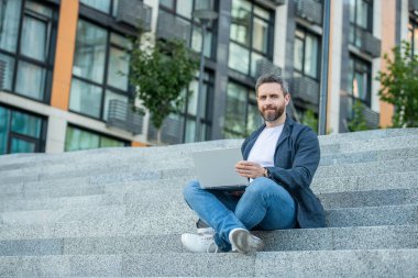 Dışarıda bilgisayar olan serbest çalışan adam için kopyalama alanı. Bilgisayarlı serbest çalışan adamın fotoğrafı. Dışarıda dizüstü bilgisayarı olan serbest çalışan bir adam. Sokaktaki serbest çalışan adam..