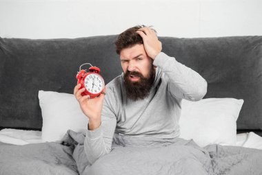 Elinde çalar saat tutan uykucu adam sabah yatağında, uyuyakalmış..