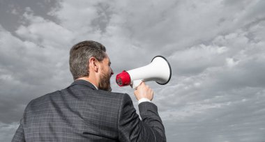 back view of businessman shout in loudspeaker on sky background. promotion.
