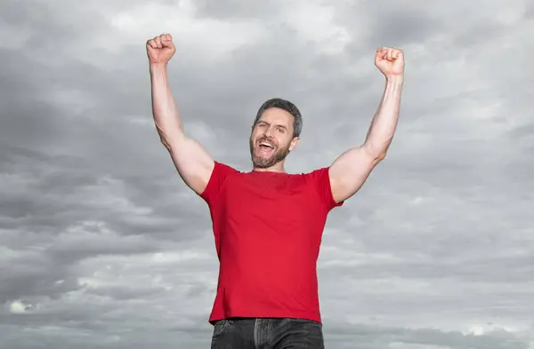 stock image Happy man making winning gesture sky background. winning guy celebrating victory keeping arms raised. Winning.