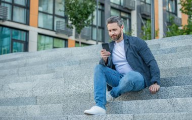 Sokakta telefonla mesajlaşan bir adam, kopyalama alanı. Dışarıda mesaj atan bir adam var. Telefonda el ele mesajlaşan bir adamın fotoğrafı. Adam dışarıda telefonla mesajlaşıyor..