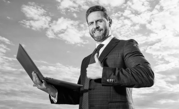 stock image Happy man specialist holding laptop. Support specialist showing thumb gesture. IT specialist smiling sky background. Successful business specialist in suit.