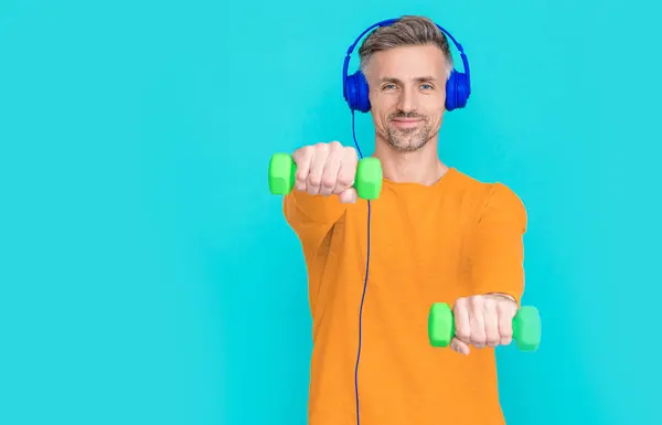 fitness man in music headphones isolated on blue, copy space. fitness man in music headphones at studio. fitness man in music headphones on background. photo of fitness man in music headphones.