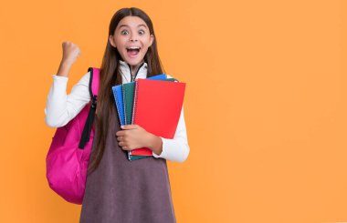 successful child with school backpack and workbook on yellow background.