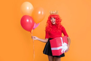 glad girl in crown with present box and party balloon on yellow background.