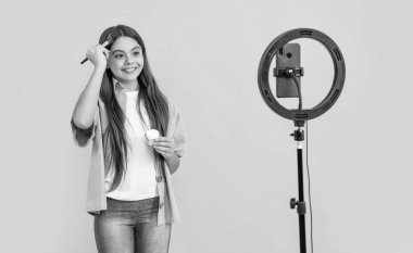 smiling teen blogger girl with brush in studio. teen blogger girl on background. photo of teen blogger girl making blog. teen blogger girl with powder isolated on yellow.