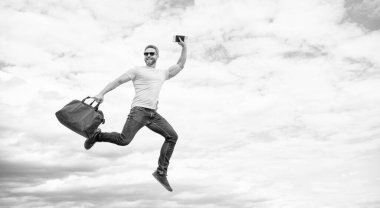 Active man jumping with travel bag midair sky background, copy space.