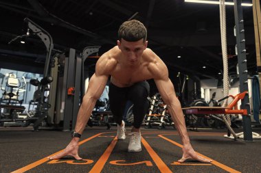 Spor salonunda başlangıç çizgisinde çömelmiş bir koşucu. Atletik adam koşu için başlangıç pozisyonunda. Spor salonunda atlet eğitimi. Spor salonunda antrenman yapmak. Spor ve zindelik.