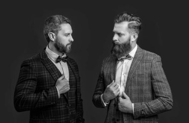 Papyonlu, resmi smokinli, beyaz, zarif erkekler. Papyonlu smokinli adamlar bordo arka planda izole edilmiş. Smokin papyonlu iki adam. Stüdyoda papyon ve smokin giyen adamlar..