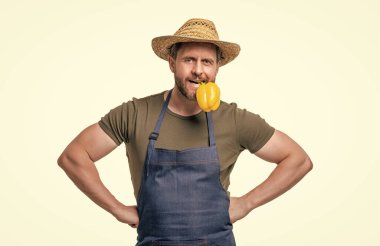 Önlüklü ve şapkalı bir adam biberli tatlı bir sebzeyi ısırıyor..