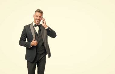 Smokinli mutlu adam beyaz arka planda izole bir şekilde telefonla konuşuyor..