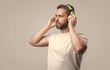 Kafkasyalı adam gri arka planda izole edilmiş kulaklıkla müzik dinliyor. Adam stüdyoda kulaklıkla müzik dinliyor. Adam modern kulaklıkla müzik dinliyor. Kulaklıkla müzik dinleyen bir adamın fotoğrafı..