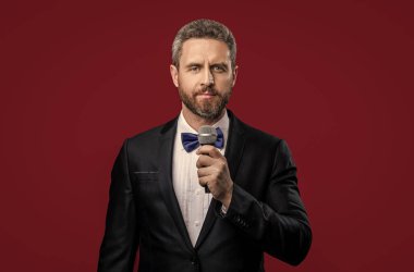 Mikrofonlu smokin adam sunucusu. Smokinli sunucunun fotoğrafı, mikrofon. Smokin sunucusu kırmızı arka planda izole edilmiş. Stüdyoda sunucu.