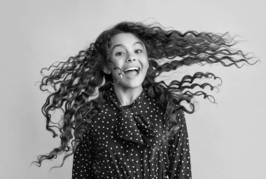 amazed girl with long brunette curly hair on yellow background.