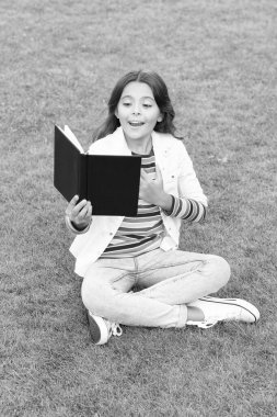 proud teen girl read book sitting on grass. reading book. reader girl with book outdoor.