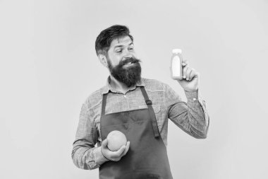 Portakal suyu şişesine bakan önlüklü mutlu adam sarı arka plan, barmen.