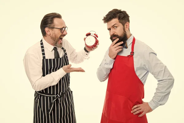It is lunch time. Men cooks with alarm clock. Man bearded hipster and mature chef apron white background. Start cooking right now. Working hours and lunch break. Lack of time. Check what time is it.