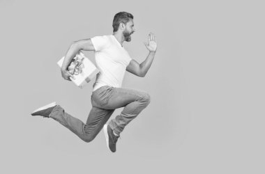 Active man running to deliver present box. Delivery boy in midair yellow studio background. Express delivery service. Fast delivery, copy space.