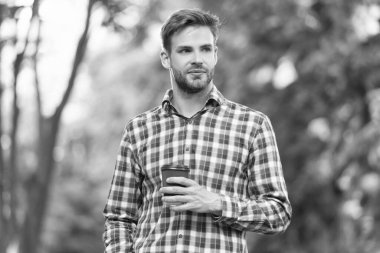 Genç adam damalı gömlekle kahve fincanı ile gülümsüyor..