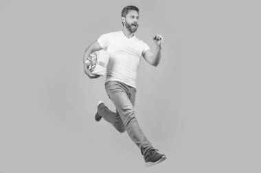 Energetic courier guy running with present box in midair yellow studio background. Courier service. Fast courier delivery.