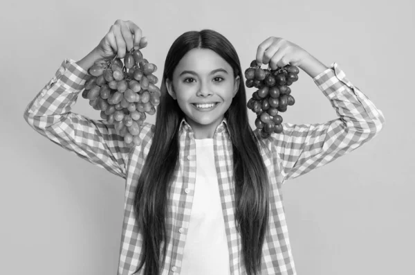 stock image cheerful teen kid with grapes bunch on yellow background.